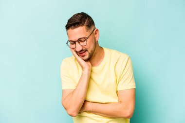 Mavi arka planda izole edilmiş genç İspanyol adam mutlu bir şekilde gülüyor ve ellerini karnının üstünde tutarak eğleniyor..