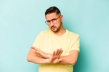 Genç İspanyol bir adam mavi arka planda izole edilmiş, inkar jesti yapıyor.