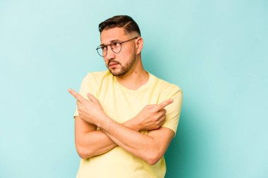 Mavi arka plan noktalarında izole edilmiş genç İspanyol adam iki seçenek arasında seçim yapmaya çalışıyor..