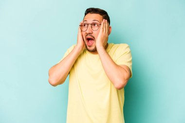 Genç İspanyol bir adam mavi arka planda izole edilmiş kulaklarını elleriyle kapatıyor çok fazla ses duymamaya çalışıyor..
