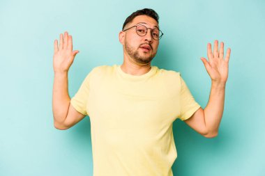 Genç İspanyol bir adam mavi arka planda izole edilmiş. Yakın bir tehlike nedeniyle şok oluyor.