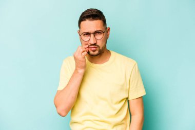 Genç İspanyol adam mavi arka planda izole edilmiş, parmakları dudaklarında bir sır saklıyor..