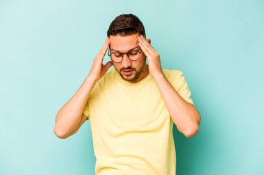 Genç İspanyol bir adam mavi arka planda izole edilmiş, başı ağrıyor, yüzüne dokunuyor..