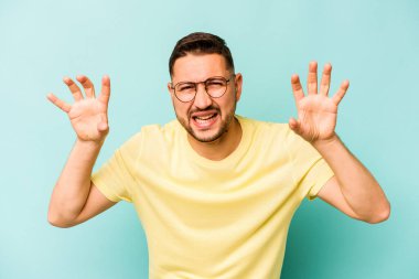 Mavi arka planda izole edilmiş genç İspanyol bir adam pençelerini bir kediyi taklit ederken gösteriyor, agresif bir hareket..