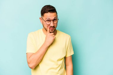 Latin kökenli genç bir adam mavi arka planda izole edilmiş. Bir strateji planlıyor, bir iş yolu düşünüyor..