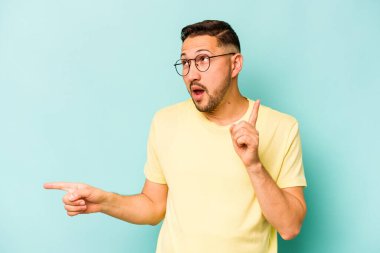 Mavi arka planda izole edilmiş genç İspanyol adam farklı kopya alanlarını gösteriyor, birini seçiyor, parmaklarıyla gösteriyor..