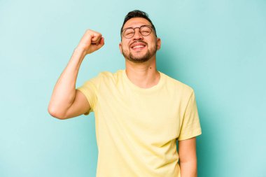 Mavi arka planda izole edilmiş genç İspanyol bir adam zaferi, tutkuyu ve coşkuyu kutluyor, mutlu bir ifade..