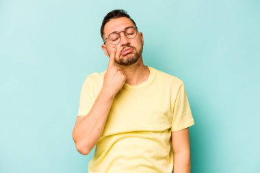 Genç İspanyol bir adam mavi arka planda izole edilmiş, ağlıyor, bir şeyden memnun değil, acı ve kafa karışıklığı konsepti..