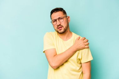 Mavi arka planda izole edilmiş genç İspanyol bir adam omuz ağrısı çekiyor..