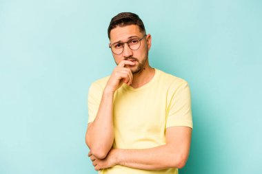 Genç İspanyol adam mavi arka planda izole edilmiş düşünüyor, bakıyor, yansıtıyor, düşünüyor, hayal kuruyor..
