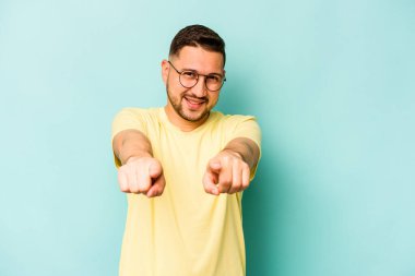 Mavi arka planda izole edilmiş genç İspanyol adam parmaklarıyla öne işaret ediyor..