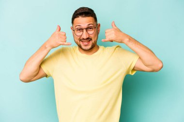 Mavi arka planda izole edilmiş genç bir İspanyol, parmakları olan bir cep telefonu hareketi gösteriyor..