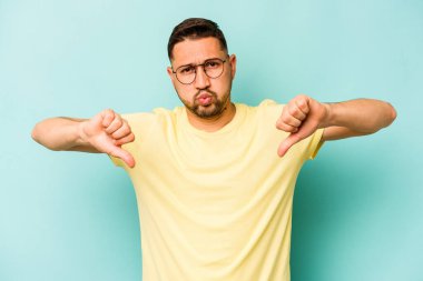 Genç İspanyol bir adam mavi arka planda izole edilmiş. Hoşlanmadığı bir hareket gösteriyor. Anlaşmazlık konsepti.