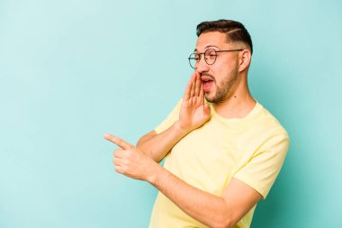 Genç İspanyol bir adam mavi arka planda izole edilmiş. Dedikodu yapıyor, bir şeyleri bildiriyor..