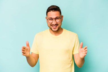 Mavi arka planda izole edilmiş genç İspanyol adam iki eliyle bir şey tutuyor, ürün sunumu..