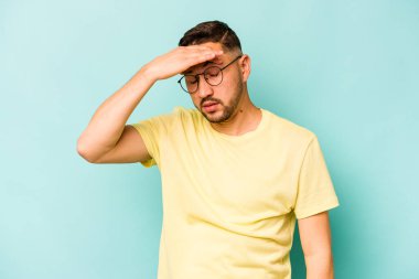 Genç İspanyol adam mavi arka planda izole edilmiş tapınaklara dokunuyor ve baş ağrısı çekiyor..