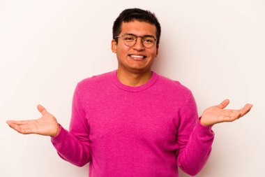 Beyaz arka planda izole edilmiş genç İspanyol adam kollarıyla ölçeği yapıyor, mutlu ve kendinden emin hissediyor..