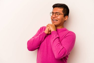 Latin kökenli genç bir adam beyaz arka planda izole edilmiş şans için dua ediyor, şaşırmış ve ağzı açık bir şekilde önüne bakıyor..