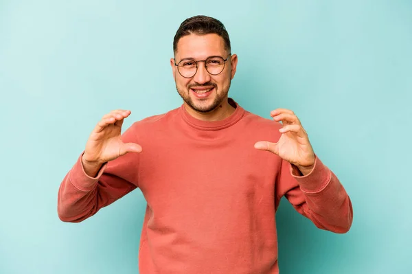 Jovem Hispânico Isolado Fundo Azul Segurando Algo Com Palmas Das — Fotografia de Stock