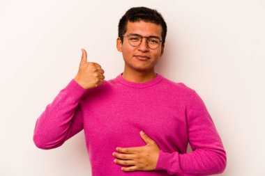 Beyaz arka planda izole edilmiş genç İspanyol adam karnına dokunuyor, nazikçe gülümsüyor, yemek yiyor ve tatmin oluyor..