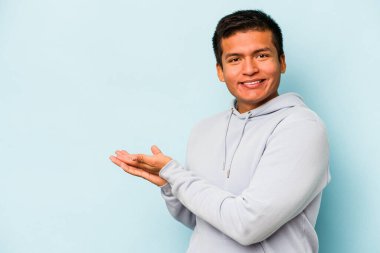 Genç İspanyol adam mavi arka planda izole edilmiş şüpheli ve şüpheci bir ifadeyle yana bakıyor..