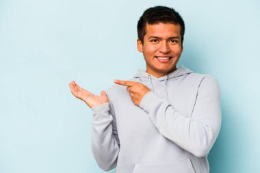 Mavi arka planda izole edilmiş genç İspanyol bir adam heyecanlı bir şekilde avuç içinde bir kopyasını tutuyor..