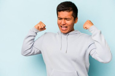Mavi arka planda izole edilmiş genç İspanyol bir adam zaferden sonra yumruk kaldırıyor, kazanan konsept..