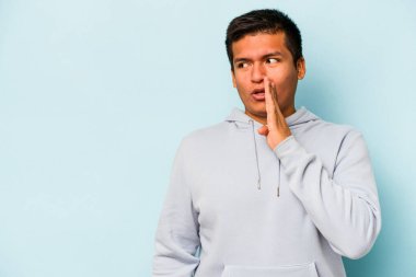 Mavi arka planda izole edilmiş genç İspanyol bir adam gizli bir sıcak fren haberi veriyor ve yana bakıyor.