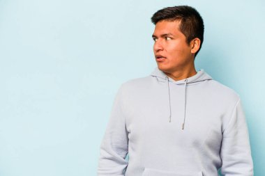 Genç İspanyol bir adam mavi arka planda izole edilmiş. Gördüğü bir şey yüzünden şok oluyor..