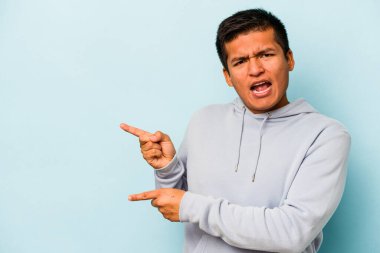 Mavi arka planda izole edilmiş genç İspanyol adam işaret parmaklarıyla fotokopi alanını işaret ederek heyecan ve arzuyu ifade ediyor..