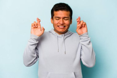 Genç İspanyol adam mavi arka planda izole edilmiş şans dilemek için şans diliyor.