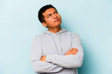 Genç İspanyol adam mavi arka planda izole edilmiş. Amaçlarına ve amaçlarına ulaşmayı hayal ediyor.