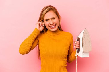 Pembe arka planda demir tutan genç beyaz kadın elleriyle kulaklarını kapatıyor..