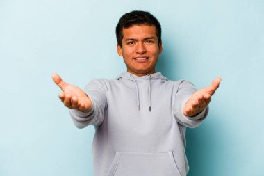 Mavi arka planda izole edilmiş genç bir İspanyol hoş geldin ifadesi sergiliyor..