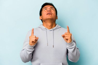 Mavi arka planda izole edilmiş genç bir İspanyol ağzı açık bir şekilde üst tarafı işaret ediyor..