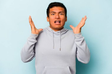Genç İspanyol adam mavi arka planda izole edilmiş gökyüzüne haykırıyor, yukarı bakıyor, hayal kırıklığına uğramış..