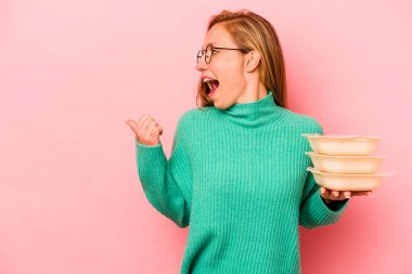 Beyaz tenli genç bir kadın pembe arka plan noktalarına izole edilmiş, baş parmak uzakta, gülüyor ve kaygısız..