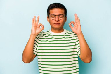 Mavi arka planda izole olmuş genç İspanyol adam sıkı çalışma gününden sonra rahatlıyor, yoga yapıyor..