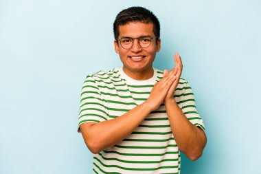 Genç İspanyol adam mavi arka planda izole edilmiş enerjik ve rahat hissediyor, ellerini ovuşturuyor kendinden emin..