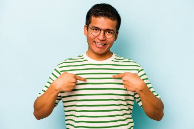 Mavi arka planda izole edilmiş genç İspanyol adam parmağını göstererek şaşırdı, geniş bir gülümsemeyle..