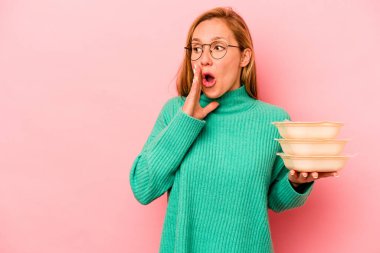 Beyaz tenli genç bir kadın pembe arka planda izole edilmiş plastik kaplar tutuyor ve gizli bir sıcak fren haberi veriyor.