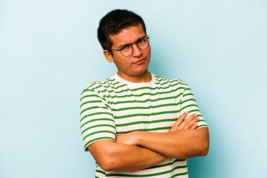 Genç İspanyol bir adam mavi arka planda izole edilmiş şüpheli, belirsiz, seni muayene ediyor..