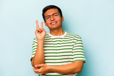 Mavi arka planda izole edilmiş genç İspanyol adam iki numarayı parmaklarıyla gösteriyor..