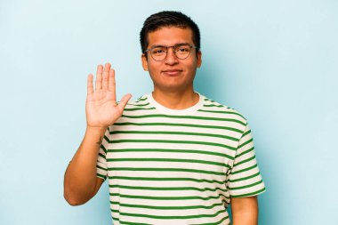 Genç İspanyol adam mavi arka planda izole edilmiş gülümsüyor beş numarayı parmaklarıyla gösteriyor..
