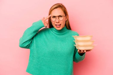 Beyaz tenli genç bir kadın pembe arka planda saklanmış vaziyette işaret parmağıyla yaptığı hayal kırıklığını gösteriyor..