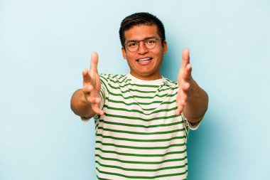 Mavi arka planda izole edilmiş genç İspanyol adam kameraya sarıldığı için kendinden emin hissediyor..