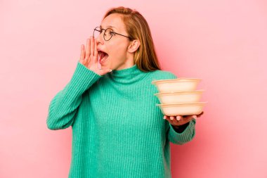 Beyaz tenli genç bir kadın pembe arka planda izole edilmiş plastik kaplar tutuyor bağırıyor ve avuç içini açık tutuyordu..