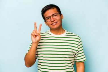 Mavi arka planda izole edilmiş genç İspanyol adam neşeli ve kaygısız parmakları olan bir barış sembolü gösteriyor..