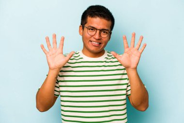 Mavi arka planda izole edilmiş genç İspanyol adam on numarayı elleriyle gösteriyor..