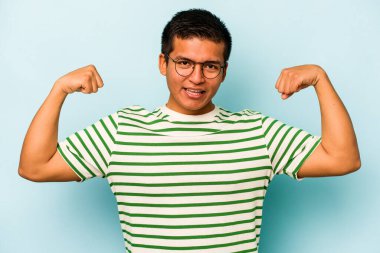 Mavi arka planda izole edilmiş genç bir İspanyol kadın gücünün sembolü olan kollarıyla güçlü bir hareket gösteriyor.